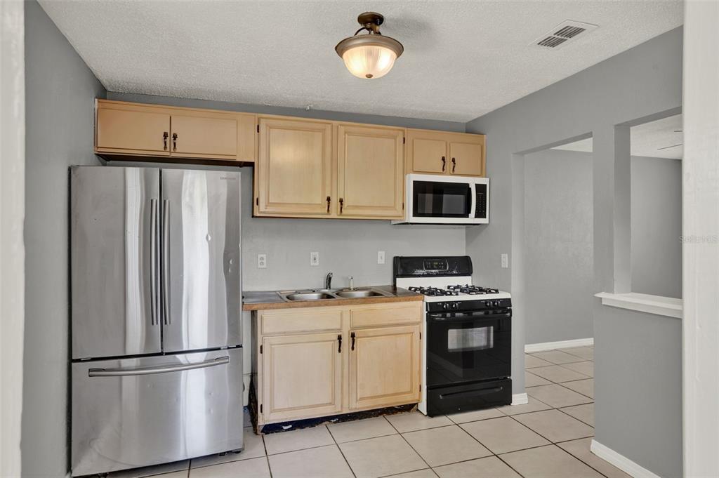 A kitchen features light wood cabinets, stainless steel appliances, and gray walls with tile flooring — 1220 MORIN STREET UNIT B, EUSTIS, FL