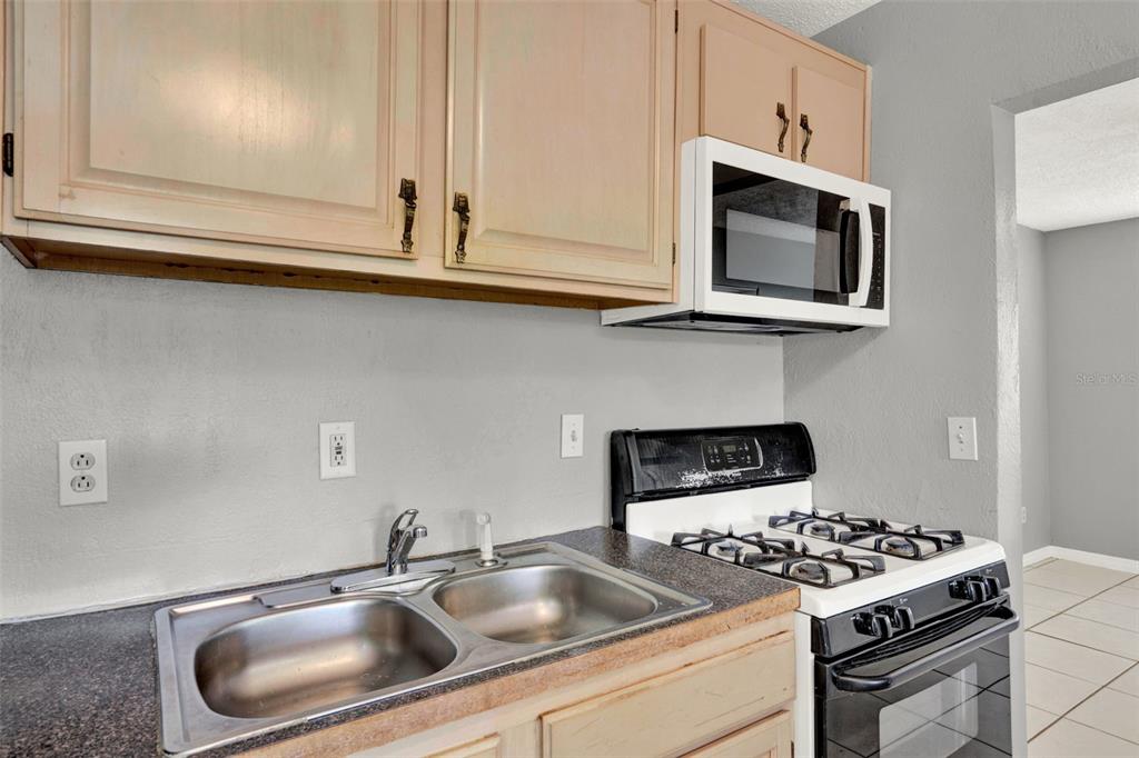 A kitchen features light wood cabinets, a stainless steel sink, and a gas range — 1220 MORIN STREET UNIT B, EUSTIS, FL