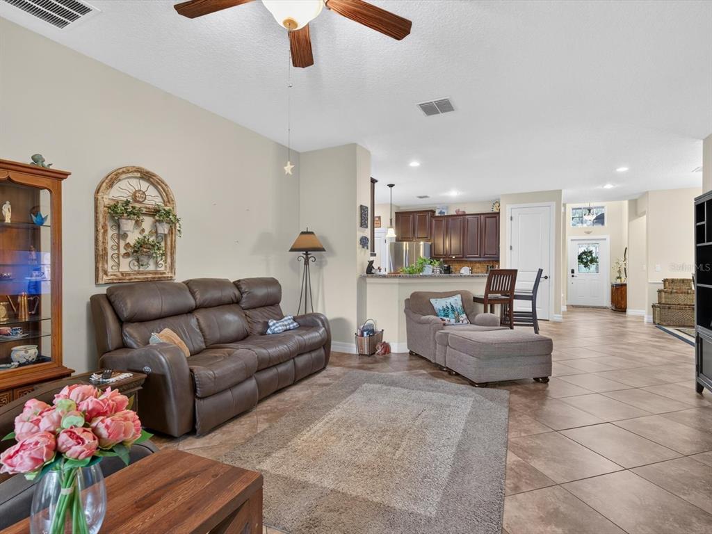 A living room with a brown leather sofa, tiled floors, and an open kitchen area — 3831 SANIBEL STREET, CLERMONT, FL