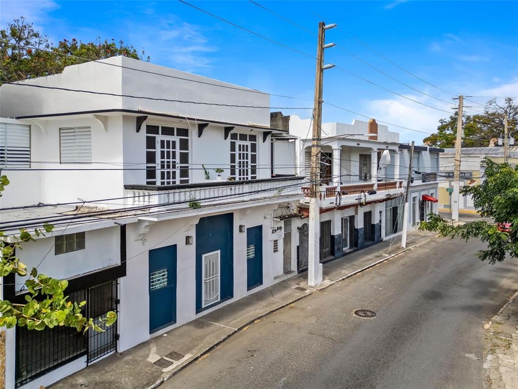 A street-level view of white two-story buildings with blue doors and balconies along a road — #159 CALLE VILLA, PONCE, PR