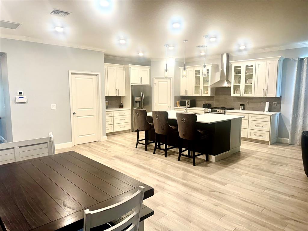 A kitchen with white cabinets, a dark island with bar seating, and light wood flooring — 5088 ENDVIEW PASS, BROOKSVILLE, FL