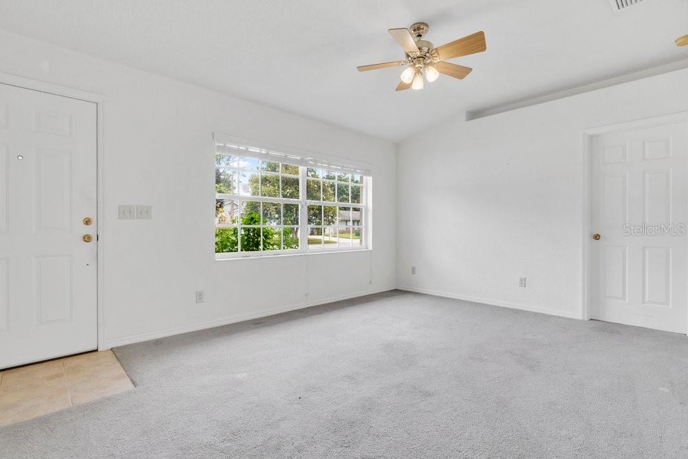 An empty room features gray carpeting, white walls, a ceiling fan, and a large window — 2225 MARYLAND AVENUE, TITUSVILLE, FL