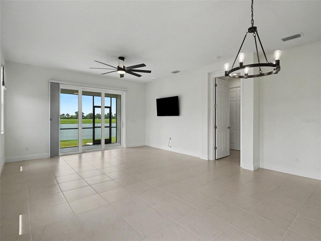 A bright living room features tile flooring, a ceiling fan, a chandelier, and sliding glass doors — 4144 GOLDEN CREEK TERRACE, PARRISH, FL