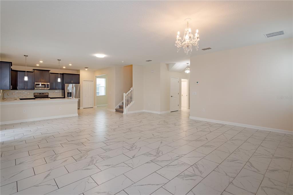 An open-concept living area features white marble-look tile flooring, a kitchen with dark cabinets, and a chandelier — 1673 MOON VALLEY DRIVE, DAVENPORT, FL