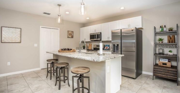 A kitchen features white cabinets, granite countertops, a stainless steel refrigerator, and three bar stools — 8643 TEMPEST DRIVE, CITRUS SPRINGS, FL