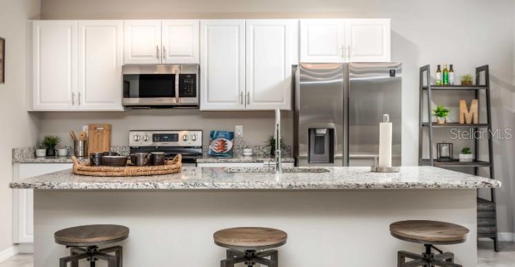 A kitchen features white cabinets, stainless steel appliances, a granite island, and three bar stools — 8643 TEMPEST DRIVE, CITRUS SPRINGS, FL