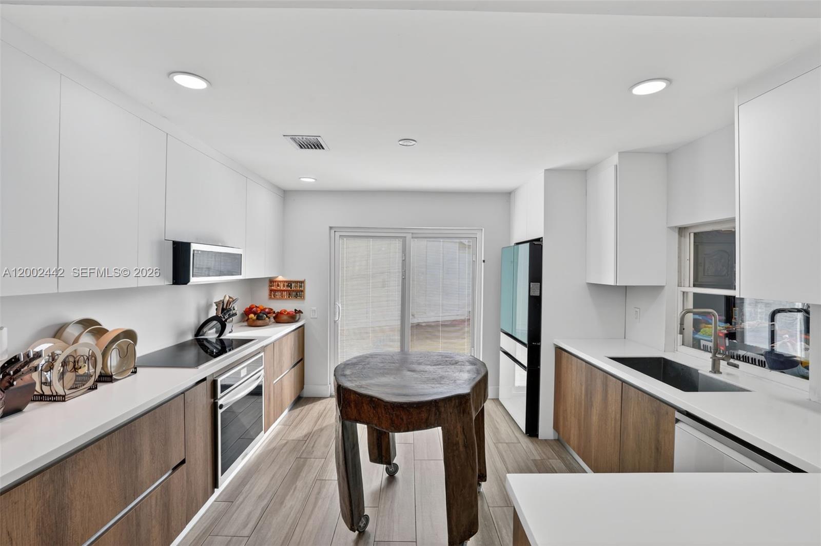 A modern kitchen features white upper cabinets, wood-grain lower cabinets, white countertops, and a central wooden island — 14914 SW 142nd Pl, Miami FL 33186, MIAMI, FL