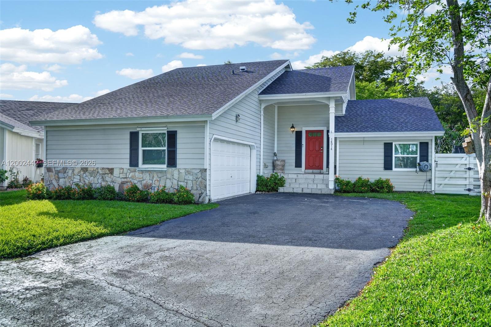 A light gray house with a stone facade, red front door, and an asphalt driveway — 14914 SW 142nd Pl, Miami FL 33186, MIAMI, FL