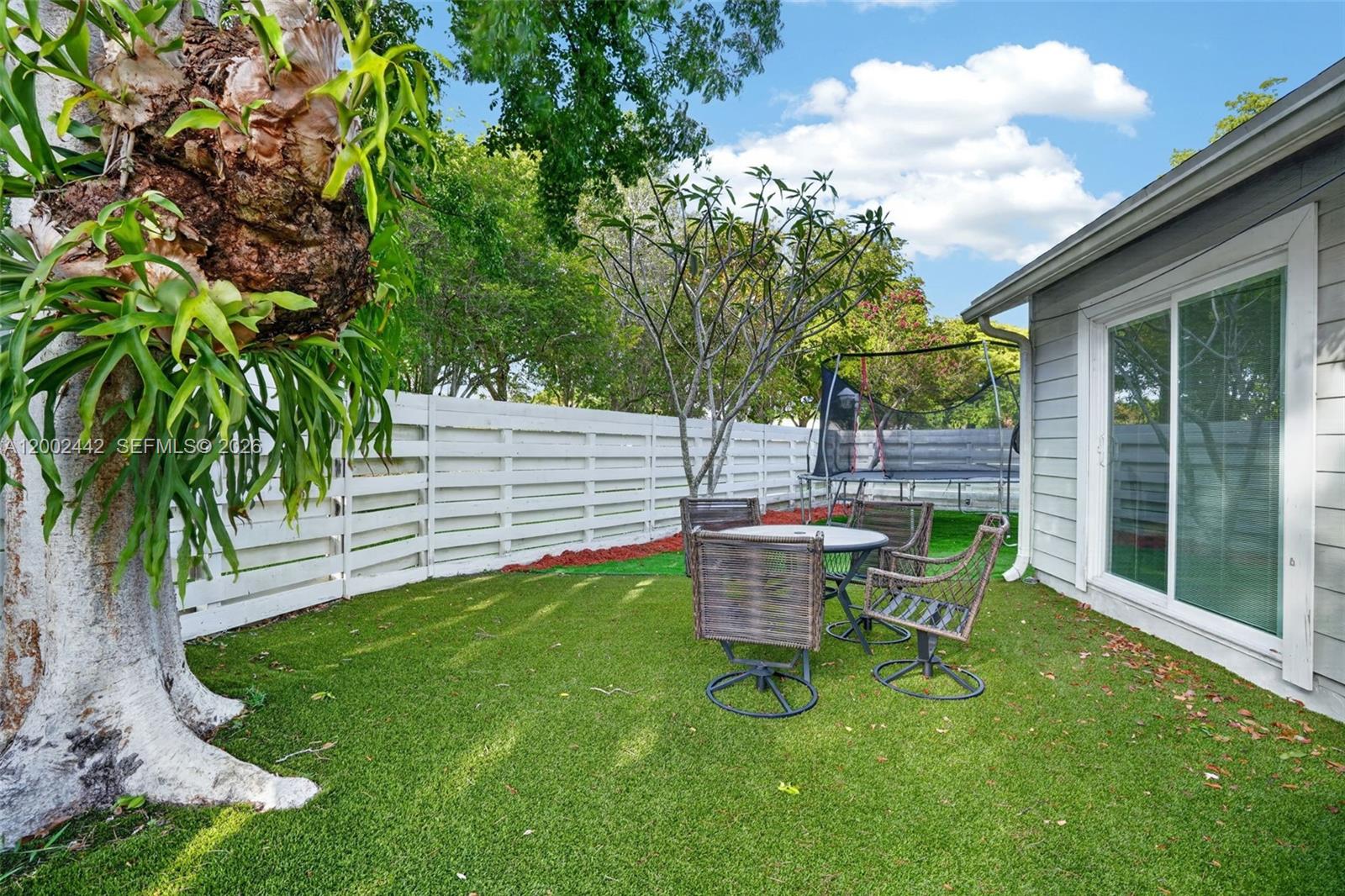 A backyard features artificial turf, a patio dining set, a trampoline, and a large tree — 14914 SW 142nd Pl, Miami FL 33186, MIAMI, FL
