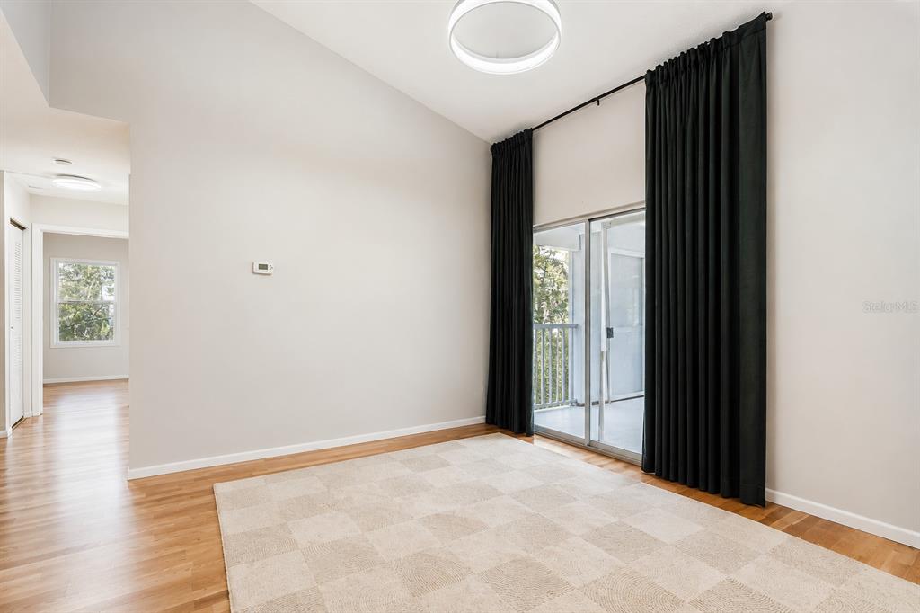 A room with light wood floors, a checkered rug, and black curtains over sliding doors — 2548 GRASSY POINT DRIVE UNIT 202, LAKE MARY, FL