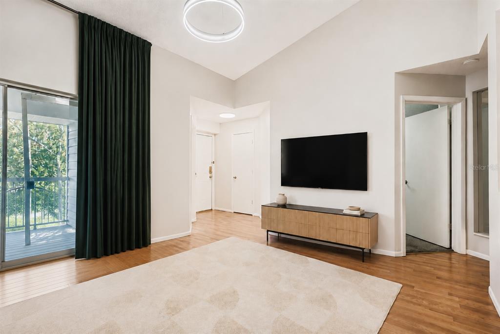 A living room features light wood flooring, a wall-mounted television, and a sliding glass door — 2548 GRASSY POINT DRIVE UNIT 202, LAKE MARY, FL