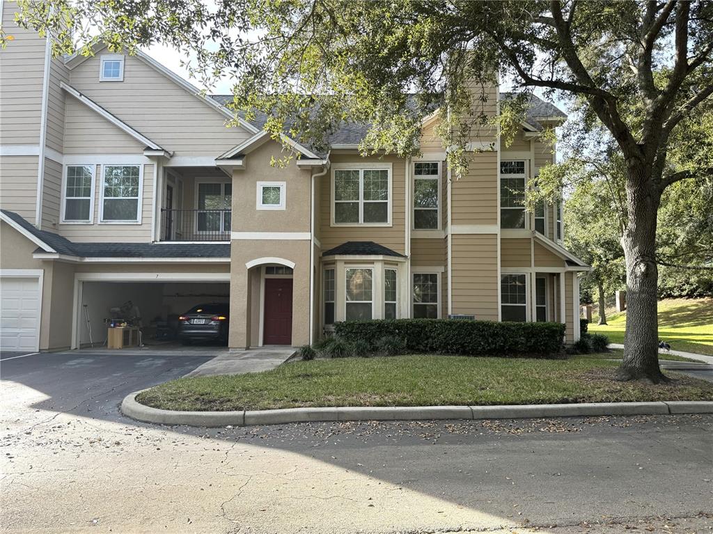 A two-story tan townhouse with a garage, red front door, and a large tree — 1101 VINTAGE VILLAGE LANE UNIT 108, OCOEE, FL