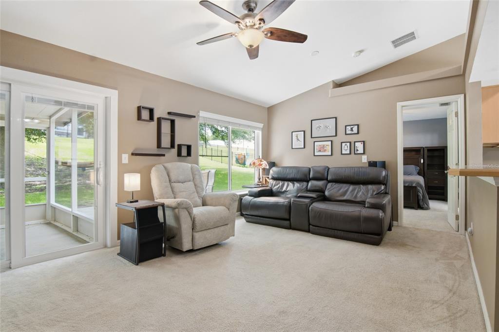 A living room with beige carpet, a leather sofa, a recliner, and a sliding glass door — 13326 PINYON DRIVE, CLERMONT, FL