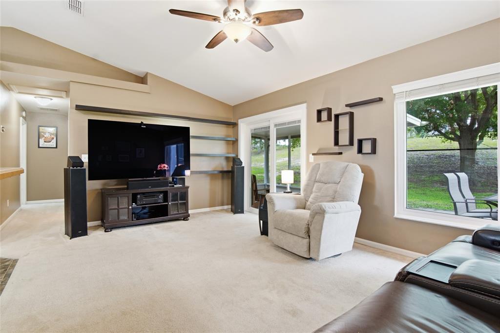 A living room features a large television, floating shelves, a recliner, and a sliding glass door — 13326 PINYON DRIVE, CLERMONT, FL