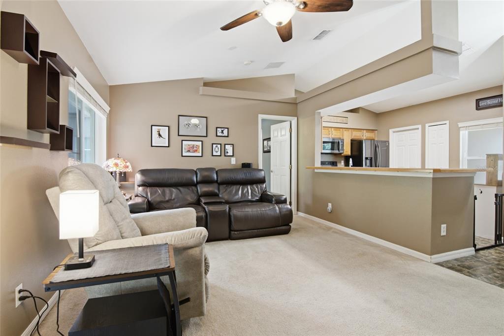 A living room with beige carpet, a leather sofa, a recliner, and an open kitchen — 13326 PINYON DRIVE, CLERMONT, FL