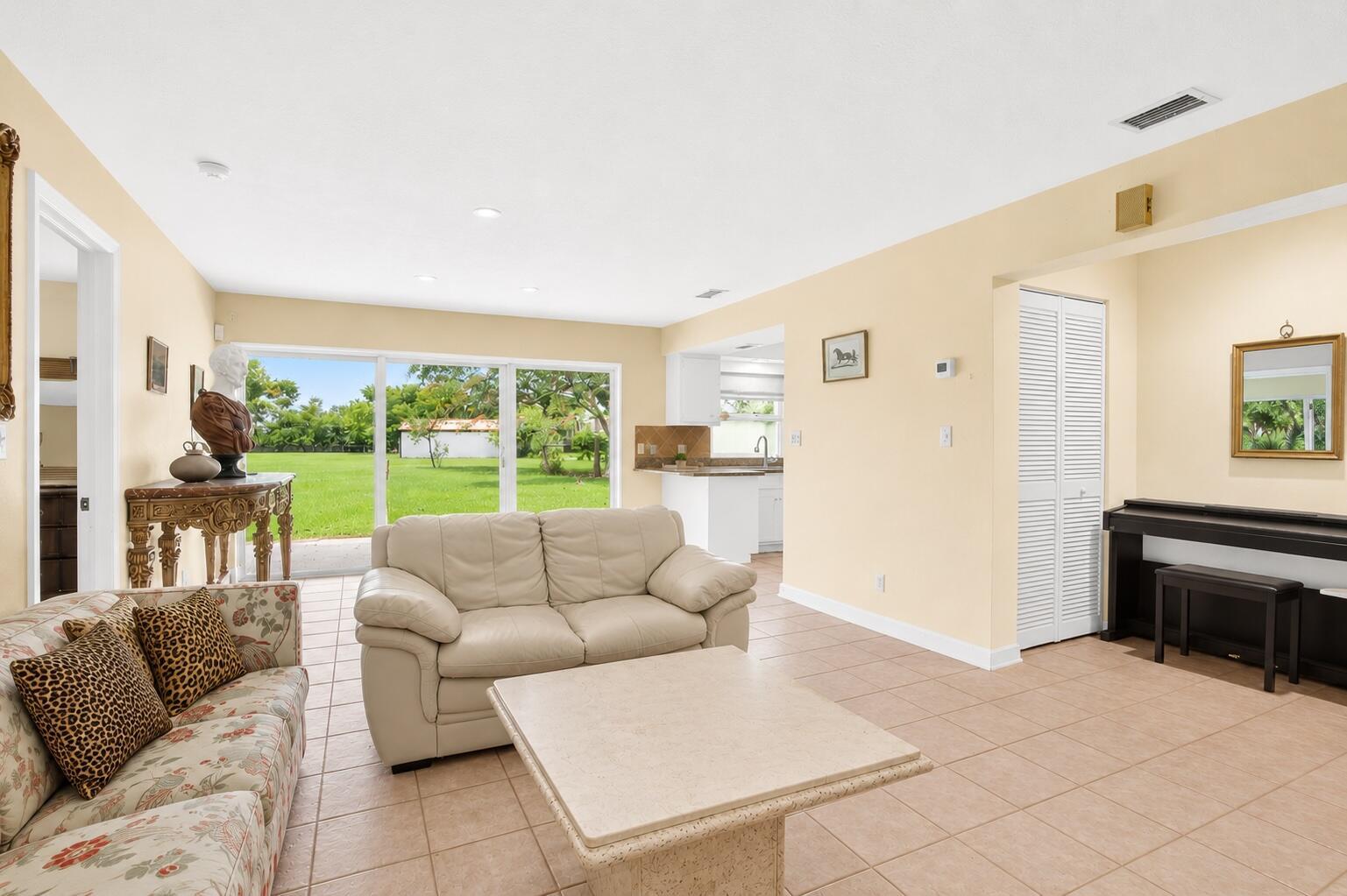 A living room with tile floors, a beige sofa, and sliding glass doors to a yard — 1029 Arabian Drive, Loxahatchee FL 33470, LOXAHATCHEE, FL
