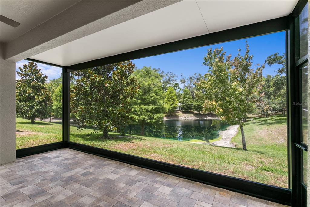 A screened-in patio with paver flooring overlooks a grassy yard and a small pond — 602 OZONA VILLAGE DRIVE, PALM HARBOR, FL