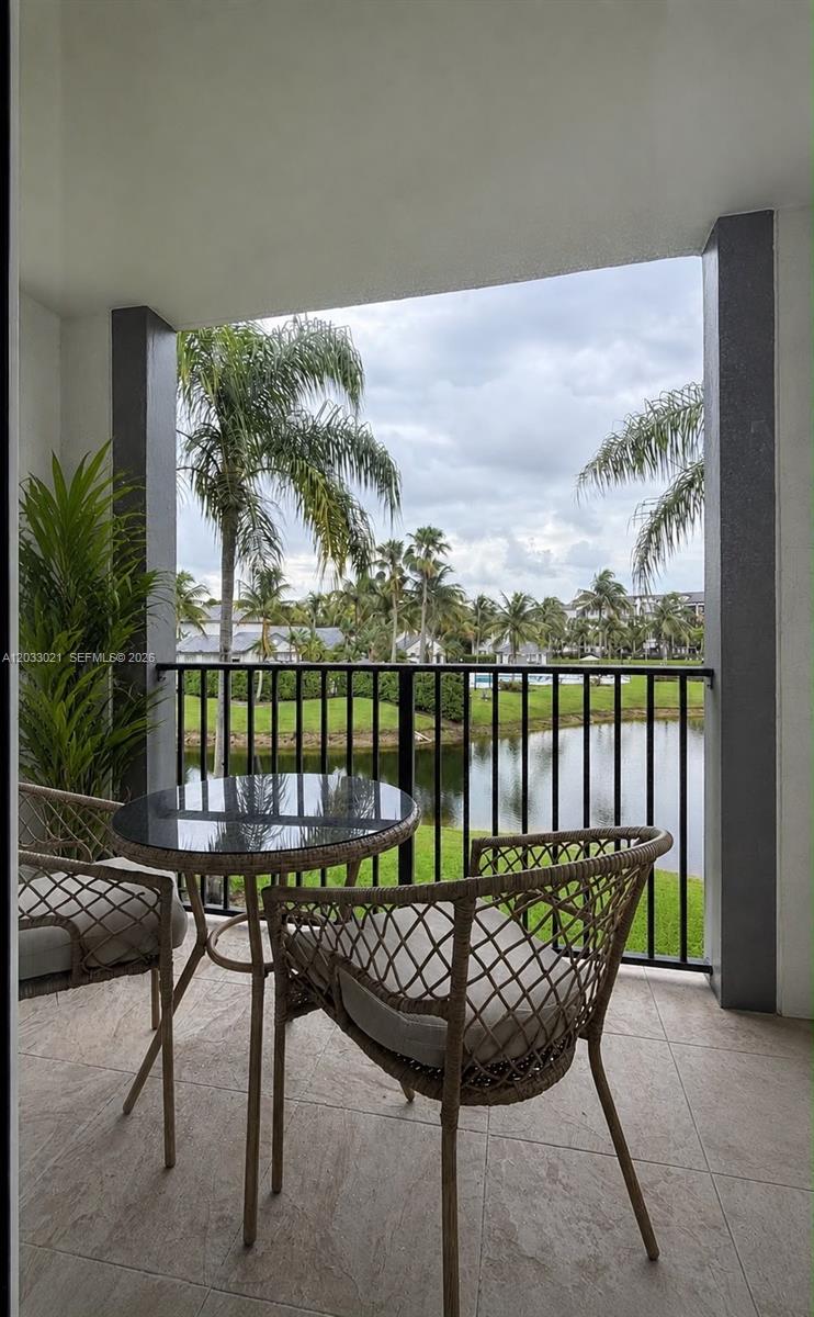 A balcony with a glass-topped table and two chairs overlooks a lake and palm trees — 4540 NW 107th Ave # 11, Doral FL 33178, DORAL, FL