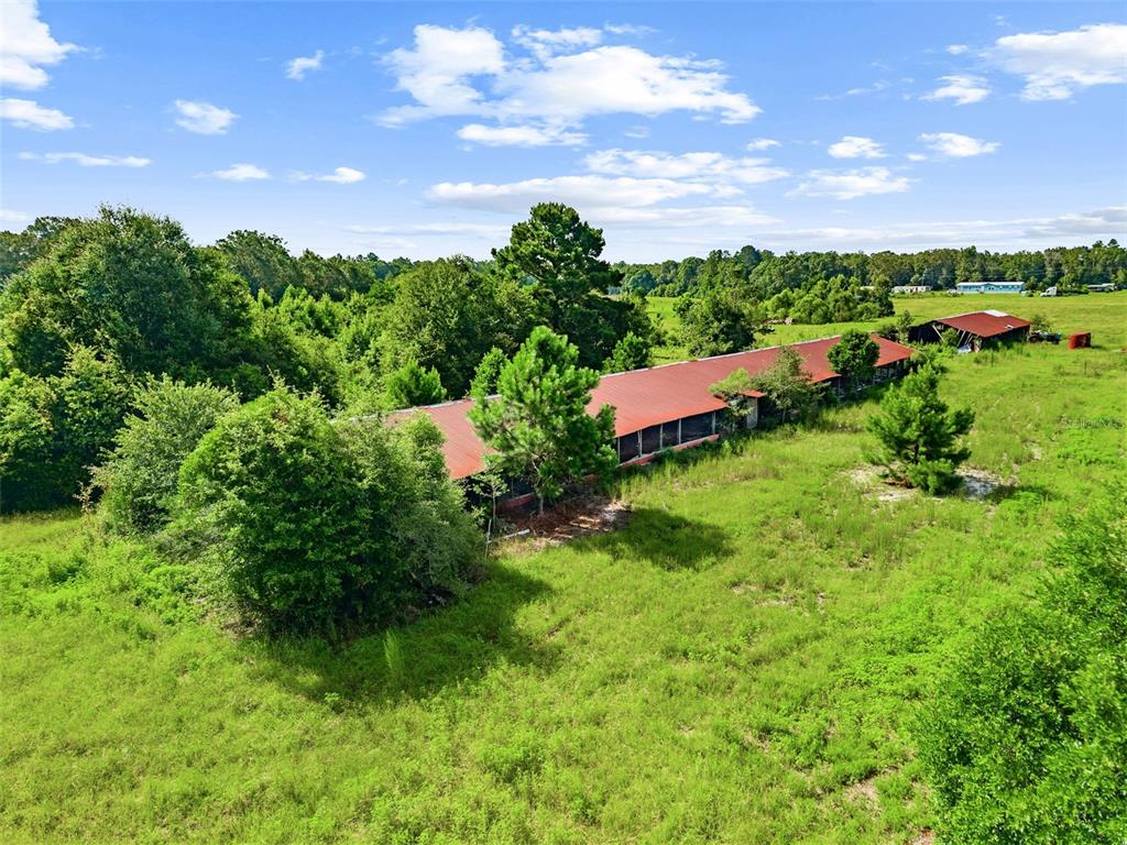 An aerial view shows a long, red-roofed agricultural building situated in a grassy field — 2853 R M WARD ROAD, PONCE DE LEON, FL