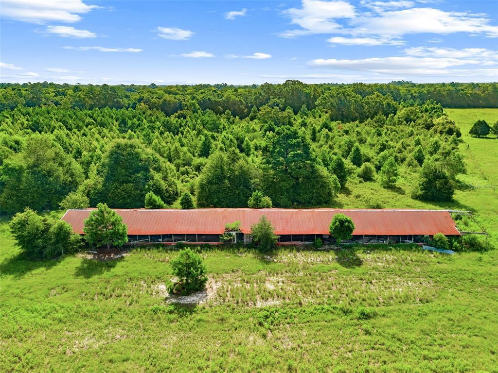 An aerial view shows a long, rusted metal-roofed agricultural building situated in a grassy field — 2853 R M WARD ROAD, PONCE DE LEON, FL