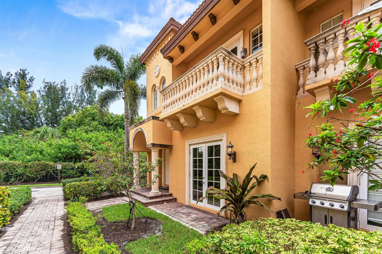 A two-story stucco house with a stone balcony, arched entryway, and a paved patio area — 210 NE 69th Circle, Boca Raton FL 33487, BOCA RATON, FL