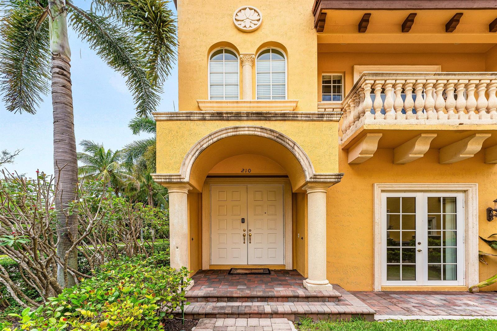 The exterior of a yellow stucco house features an arched entryway with double doors — 210 NE 69th Circle, Boca Raton FL 33487, BOCA RATON, FL