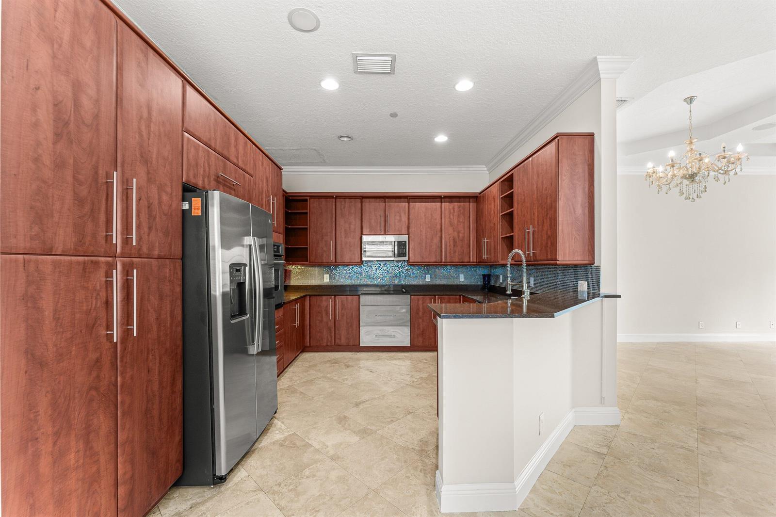 A kitchen features cherry wood cabinets, stainless steel appliances, and a blue mosaic tile backsplash — 210 NE 69th Circle, Boca Raton FL 33487, BOCA RATON, FL