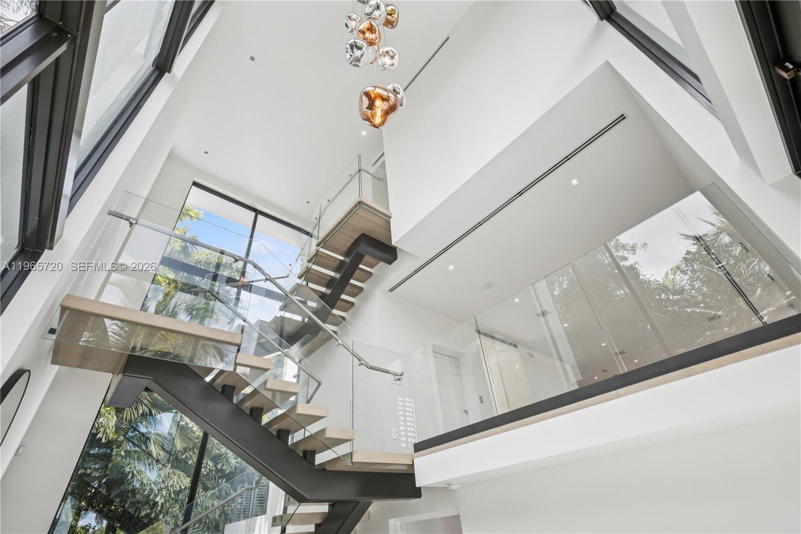 A modern staircase with glass railings and wood treads sits in a bright, multi-story foyer — 420 N Hibiscus Dr, Miami Beach FL 33139, MIAMI BEACH, FL