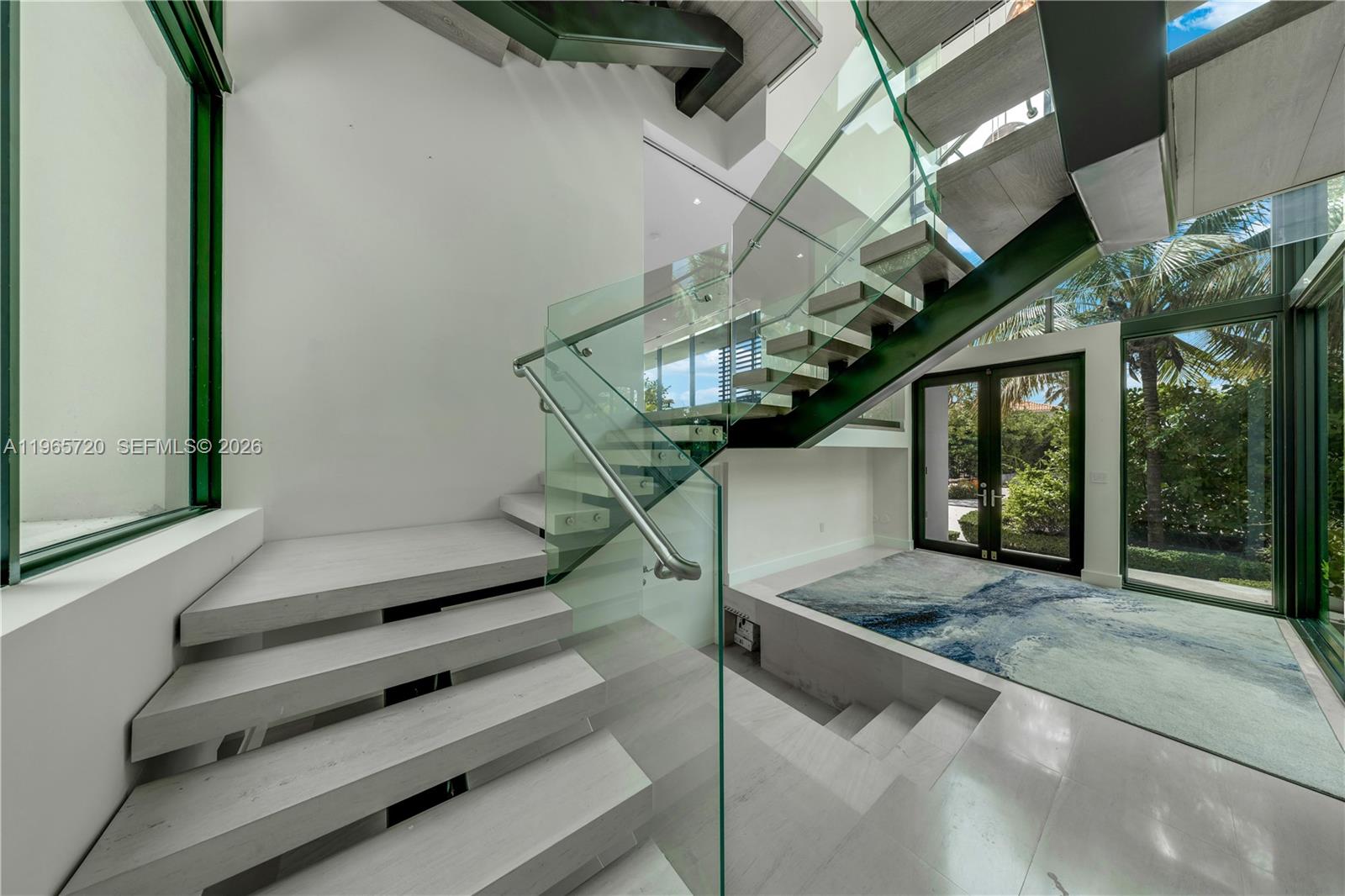 A modern foyer features a floating staircase with glass railings and a sunken seating area — 420 N Hibiscus Dr, Miami Beach FL 33139, MIAMI BEACH, FL