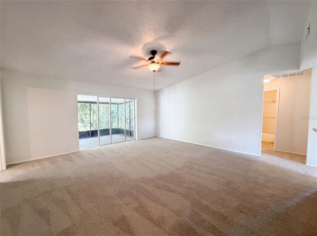 A spacious living room features beige carpeting, a ceiling fan, and sliding glass doors — 5720 KNEELAND LANE, TAMPA, FL