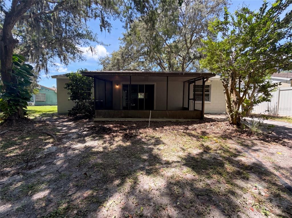 A rear view of a house featuring a screened-in porch and a sandy backyard — 5720 KNEELAND LANE, TAMPA, FL