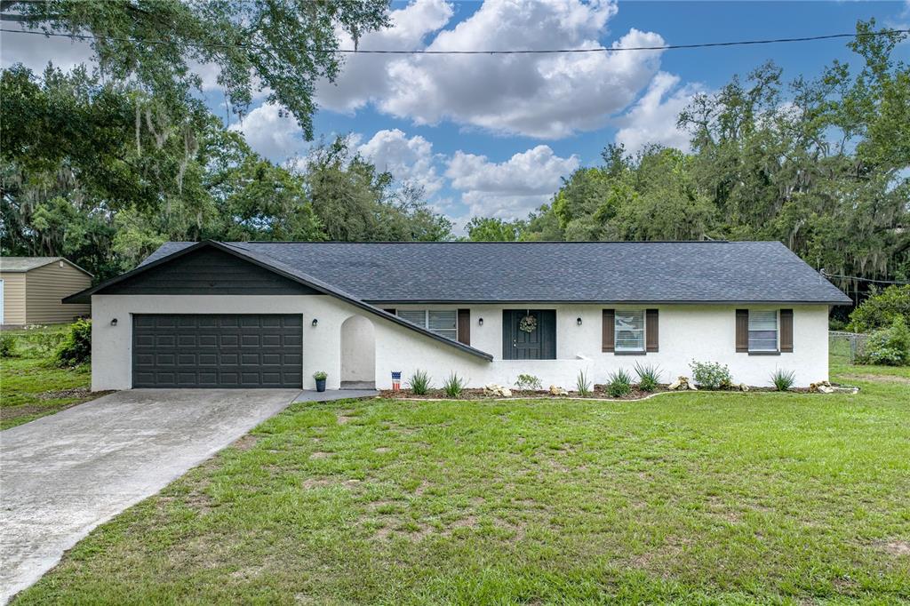 A single-story white house with a dark roof, garage, and front entrance — 37320 MOORE DRIVE, DADE CITY, FL