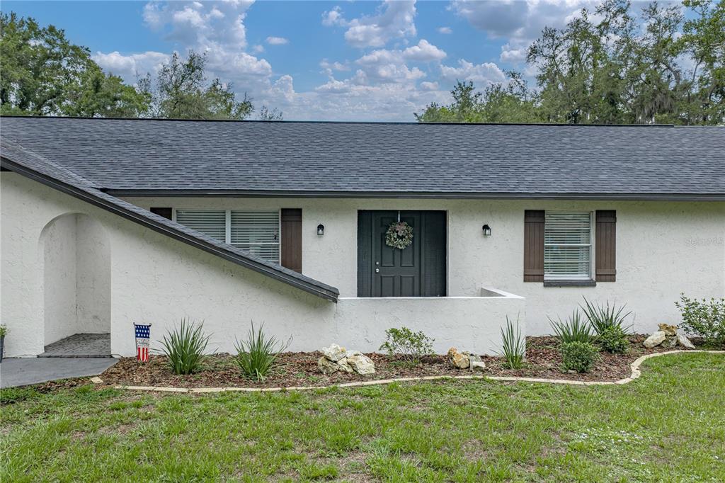 The exterior of a white stucco house features a dark front door and brown shutters — 37320 MOORE DRIVE, DADE CITY, FL