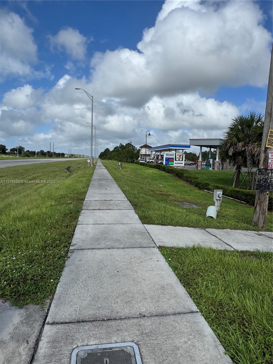 A concrete sidewalk runs alongside a grassy area leading toward a gas station — 861 BARCIA, Lehigh Acres FL 33974, LEHIGH ACRES, FL