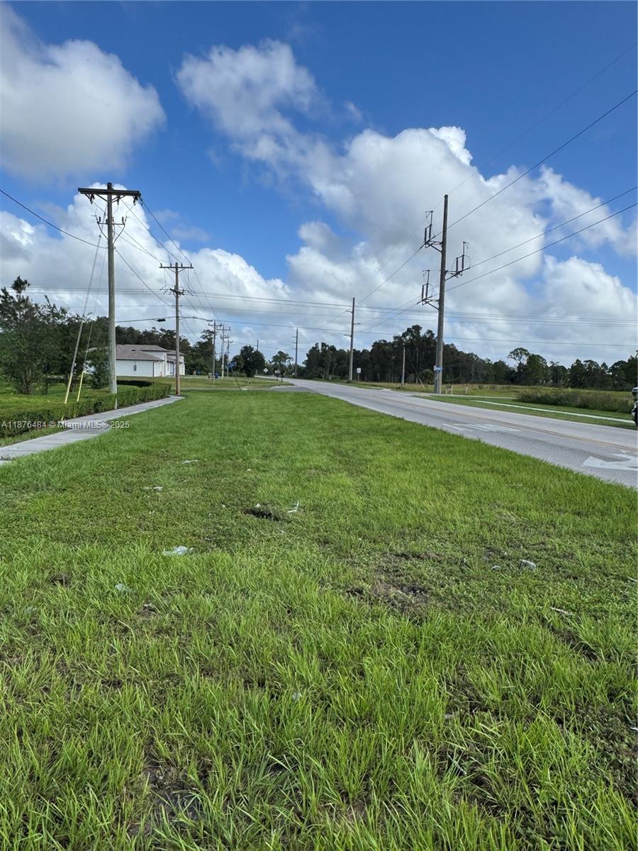A grassy roadside verge stretches toward a distant house under a bright, cloudy sky — 861 BARCIA, Lehigh Acres FL 33974, LEHIGH ACRES, FL