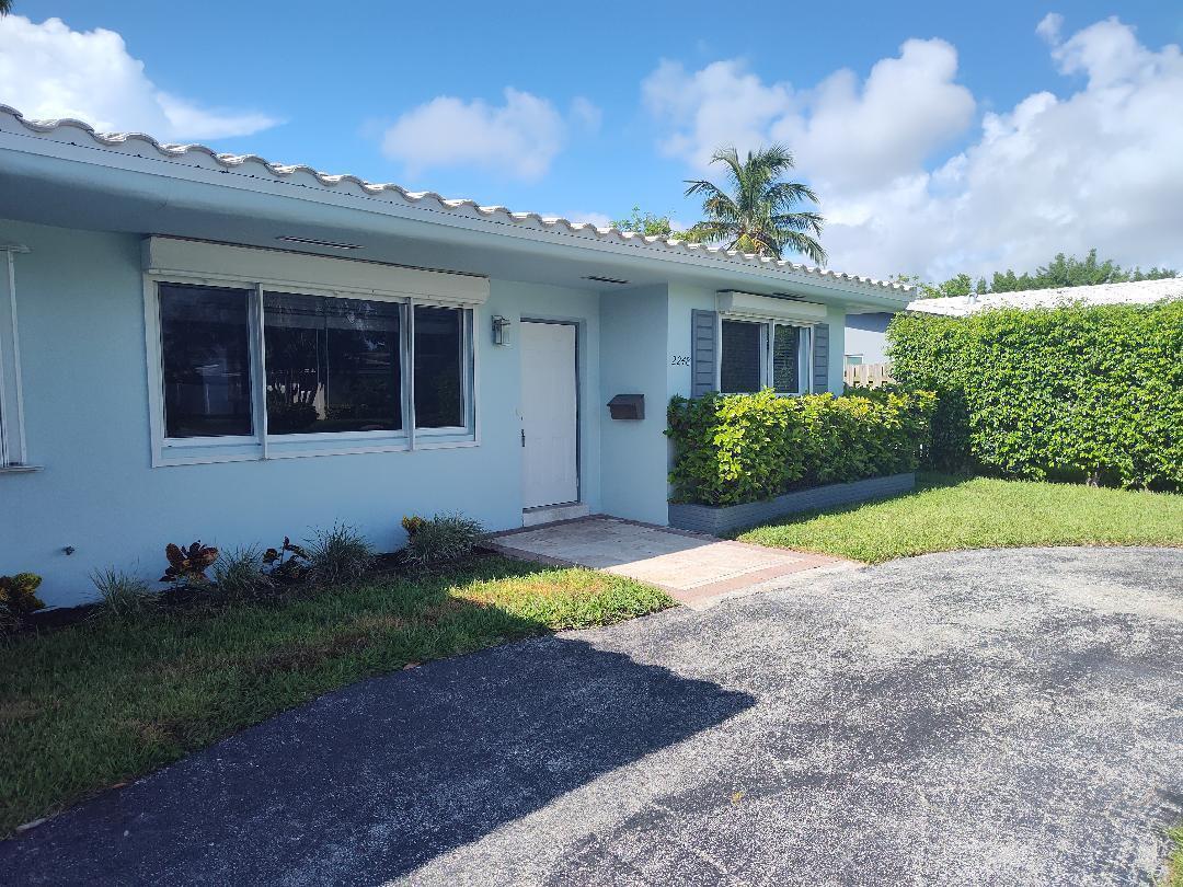 A light blue single-story house features a white front door, windows, and a paved driveway — 2248 NE 37th Street, Lighthouse Point FL 33064, LIGHTHOUSE POINT, FL