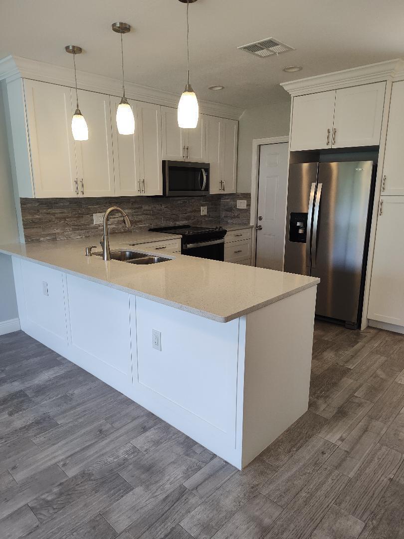 A modern kitchen features white cabinets, a quartz island countertop, and grey wood-look flooring — 2248 NE 37th Street, Lighthouse Point FL 33064, LIGHTHOUSE POINT, FL