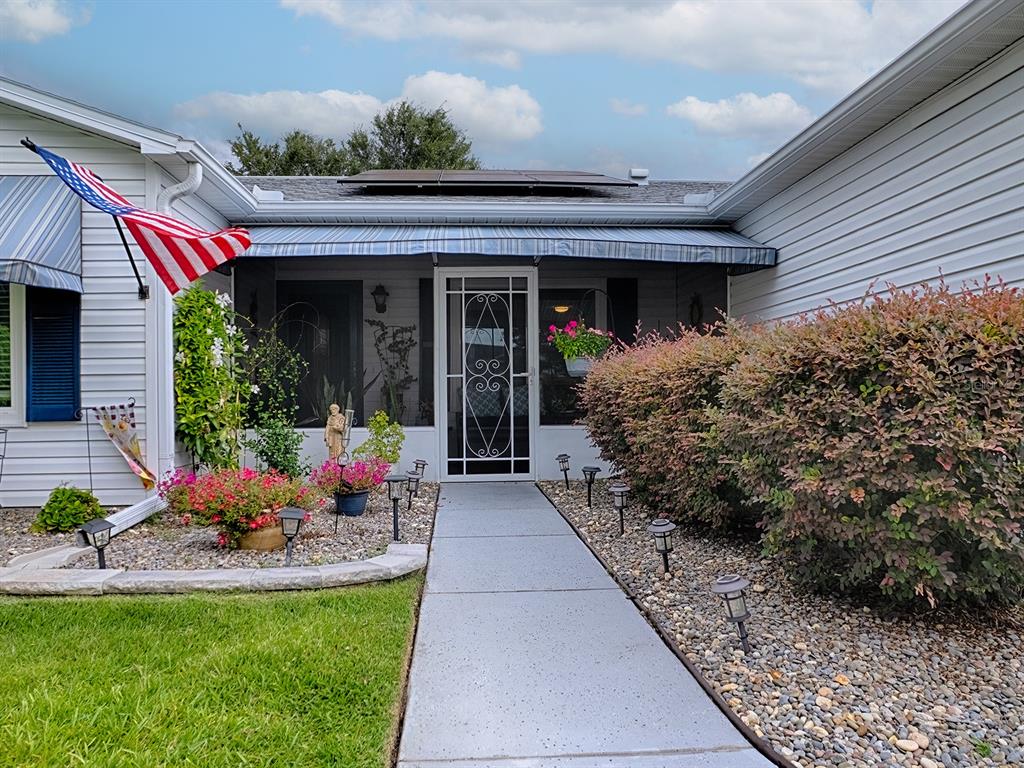 A concrete walkway leads to the screened front entrance of a house with solar panels — 1507 GARDENA COURT, THE VILLAGES, FL