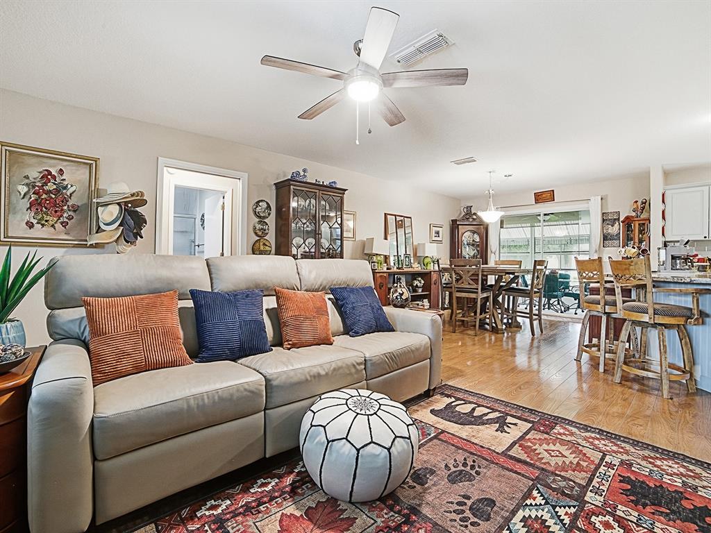 A living room with a light-colored sofa, patterned area rug, and an open dining area — 1507 GARDENA COURT, THE VILLAGES, FL