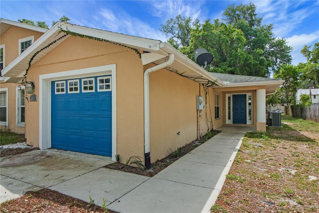 A tan house exterior features a blue garage door, a front entrance, and a walkway — 305 W FOUNTAIN STREET, FRUITLAND PARK, FL