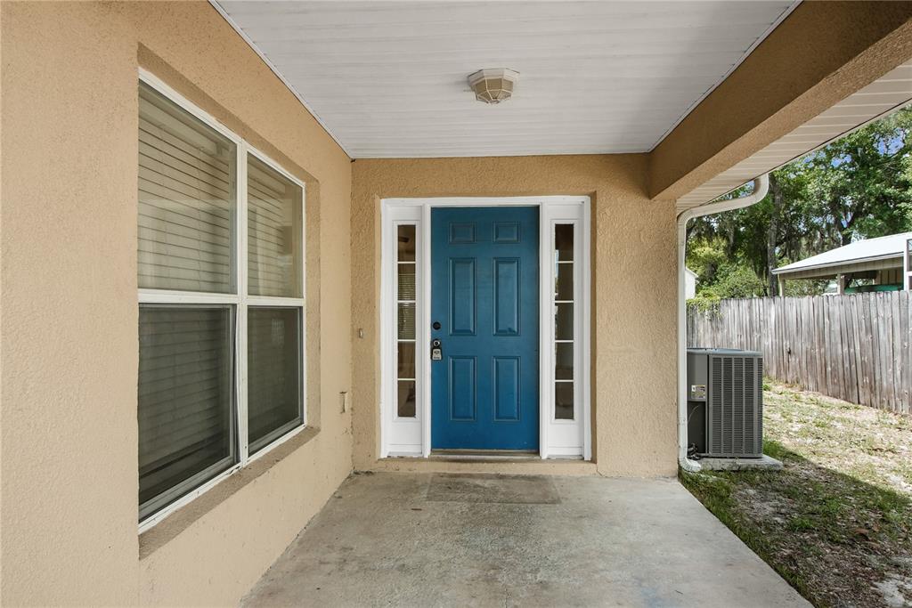 A covered concrete porch features a blue front door with sidelights and a large window — 305 W FOUNTAIN STREET, FRUITLAND PARK, FL