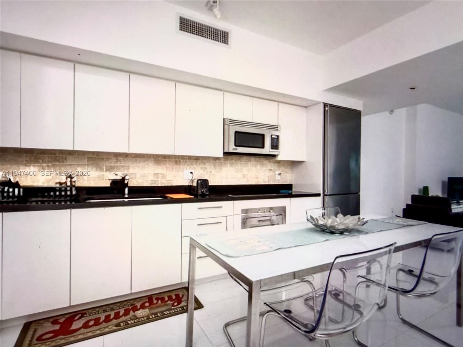 A kitchen features white cabinetry, black countertops, stainless steel appliances, and a dining table — 92 SW 3rd St # 4309, Miami FL 33130, MIAMI, FL