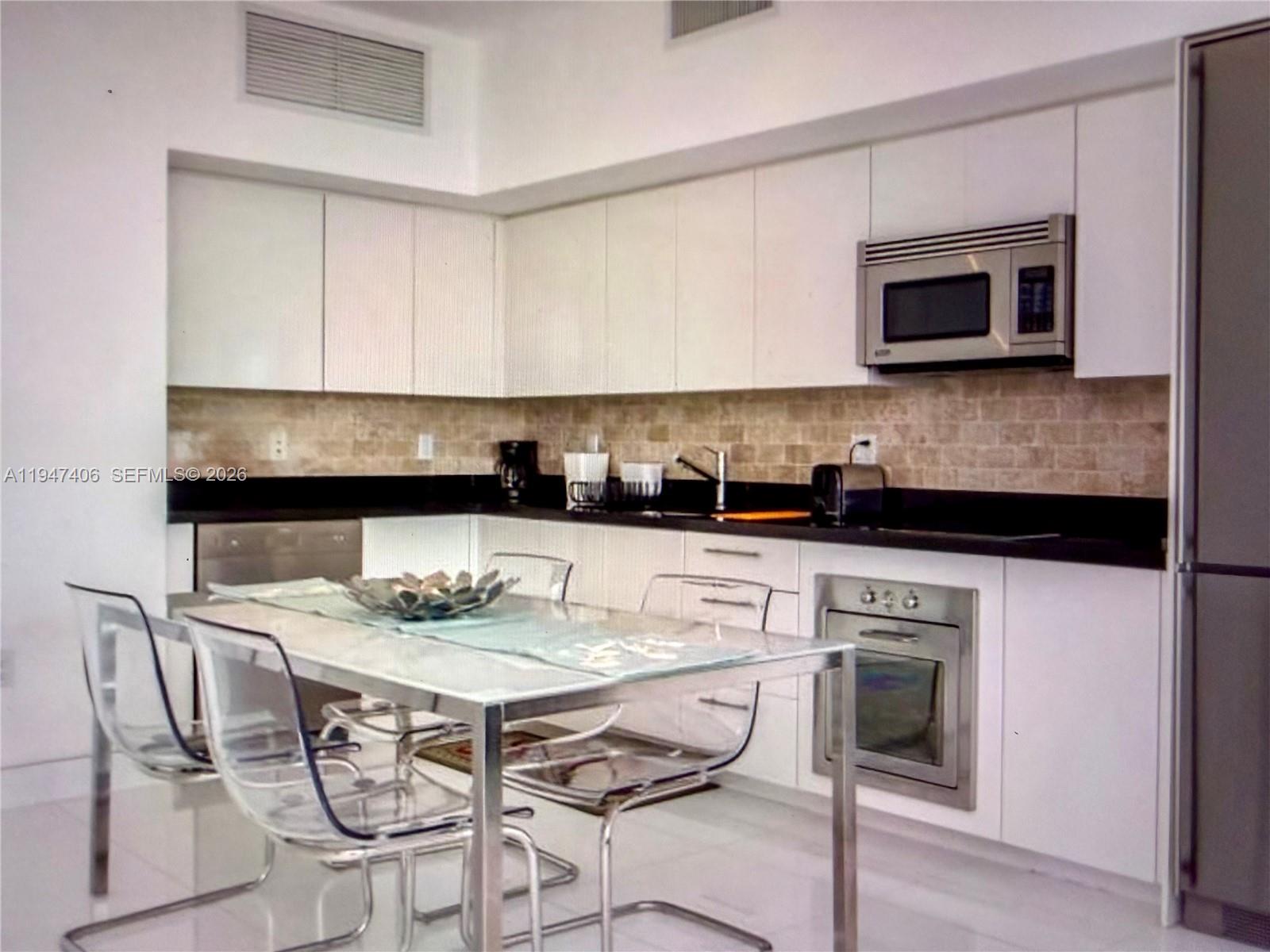 A kitchen features white cabinetry, black countertops, a glass dining table, and transparent chairs — 92 SW 3rd St # 4309, Miami FL 33130, MIAMI, FL