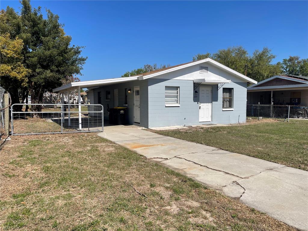 A light blue, single-story house features a concrete driveway, a carport, and a white door — 309 CENTER STREET, AUBURNDALE, FL