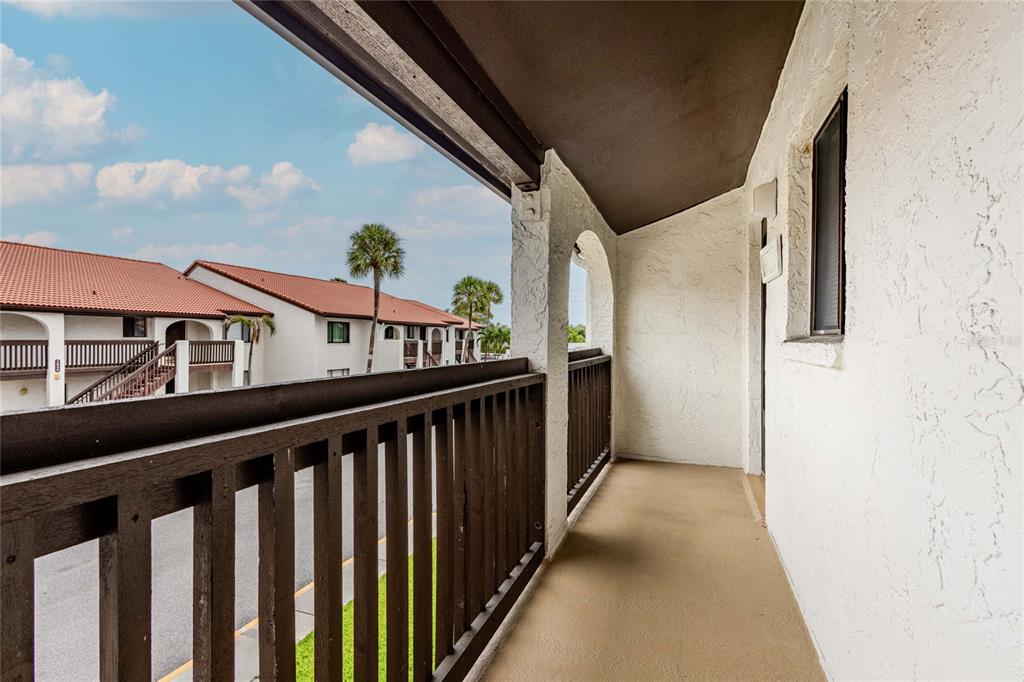An outdoor balcony with a dark wooden railing overlooks a neighboring building with palm trees — 1640 STICKNEY POINT ROAD UNIT 201, SARASOTA, FL