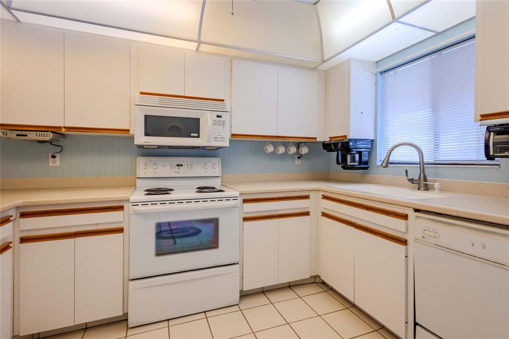 A kitchen with white cabinets, white appliances, a tiled floor, and a window with blinds — 1640 STICKNEY POINT ROAD UNIT 201, SARASOTA, FL