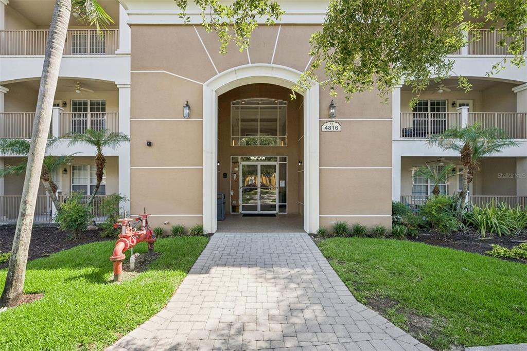 A paved walkway leads to the arched entrance of a multi-story tan apartment building — 4816 CAYVIEW AVENUE UNIT 40111, ORLANDO, FL