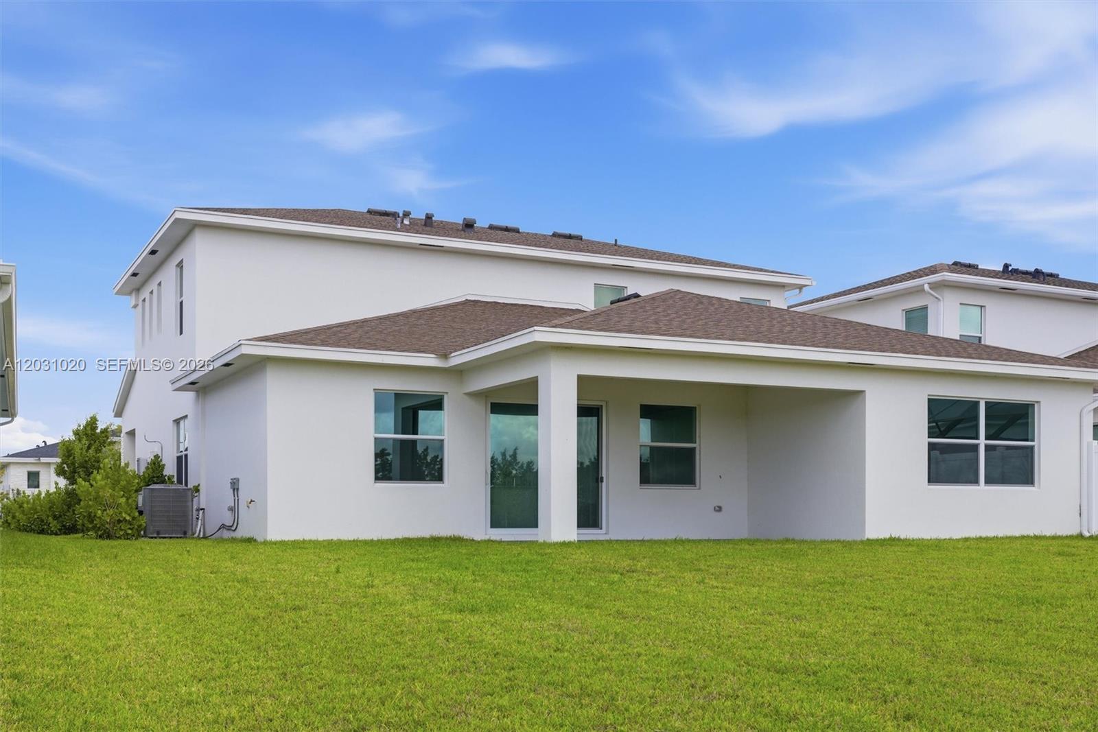 The back exterior of a two-story white house features a covered patio and a grassy yard — 1548 Stockbridge St, Loxahatchee FL 33470, LOXAHATCHEE, FL
