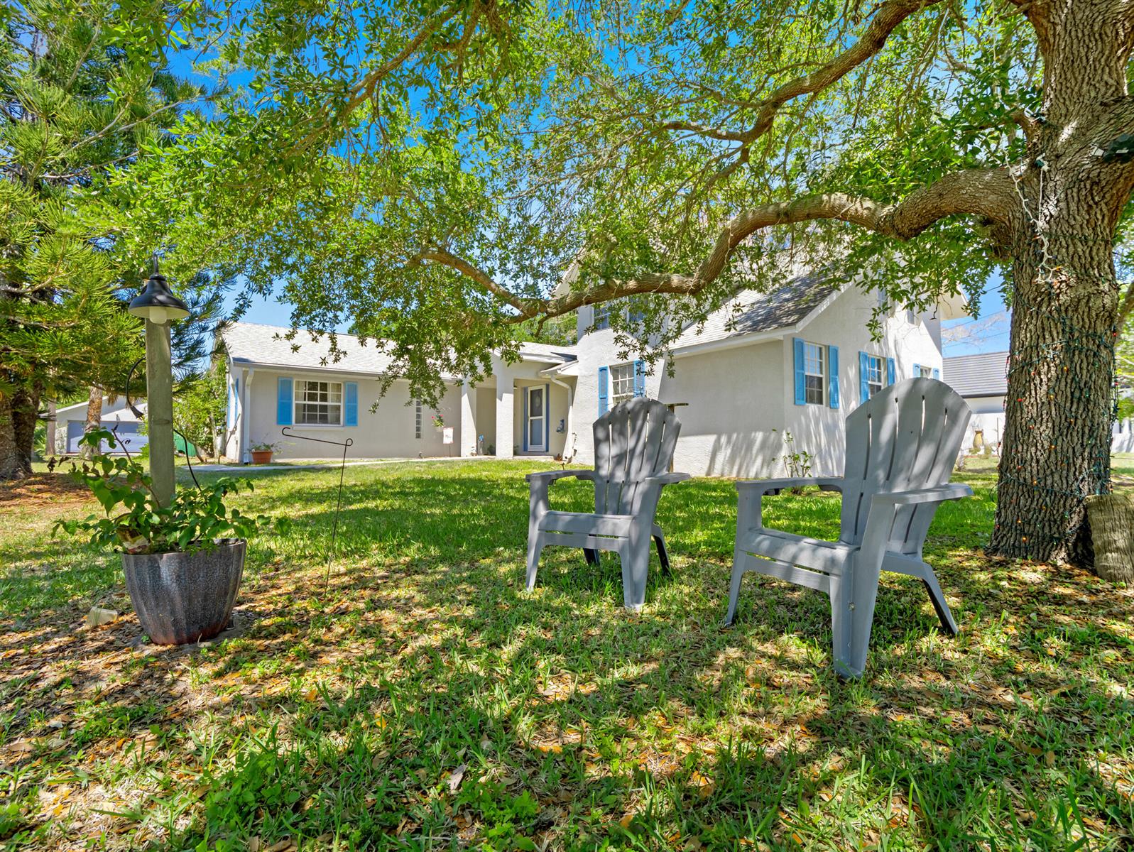 A white house with blue shutters sits behind two gray Adirondack chairs under a tree — 532 Sunset Boulevard, Melbourne Beach FL 32951, MELBOURNE BEACH, FL