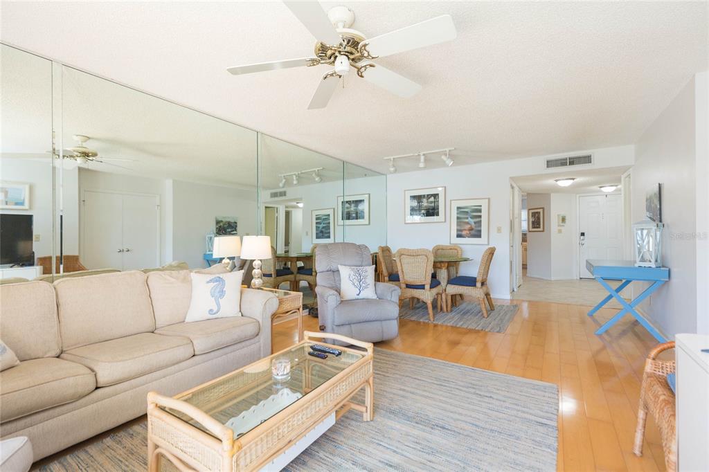 A living room with a beige sofa, wicker coffee table, mirrored wall, and dining area — 6080 BAHIA DEL MAR CIRCLE UNIT 113, ST PETERSBURG, FL
